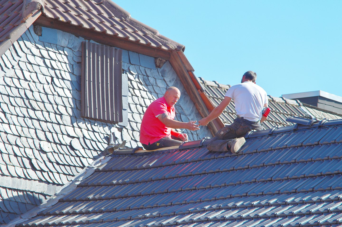 Two roofers working on a house with grey tiles.