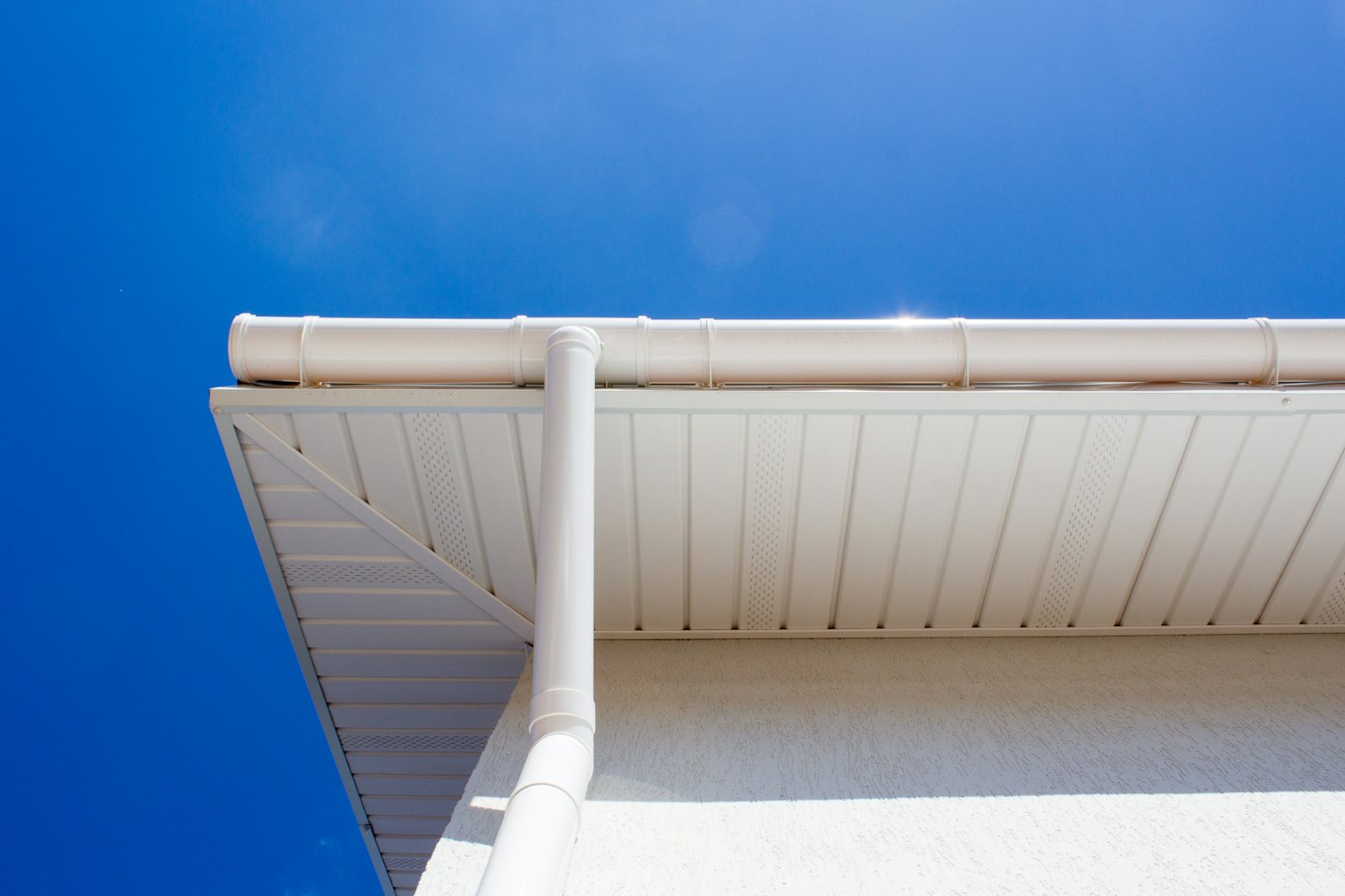 Modern house white gutter and downspout against blue sky.