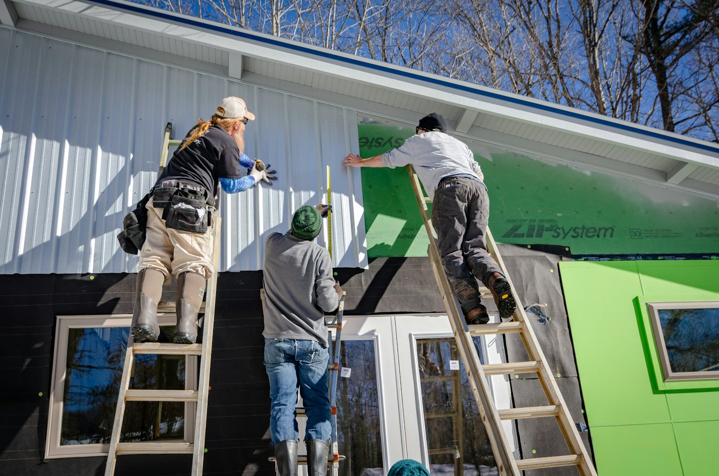 Construction workers installing corrugated metal siding on a building.